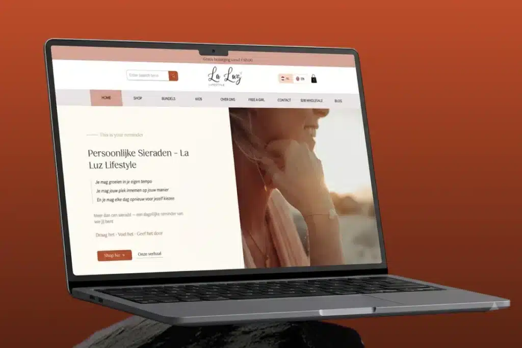 Laptop open to a La Luz Lifestyle webpage on a warm orange background, balanced on a person's shoulder/neck area.