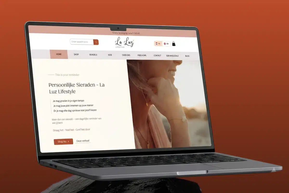 Laptop open to a La Luz Lifestyle webpage on a warm orange background, balanced on a person's shoulder/neck area.